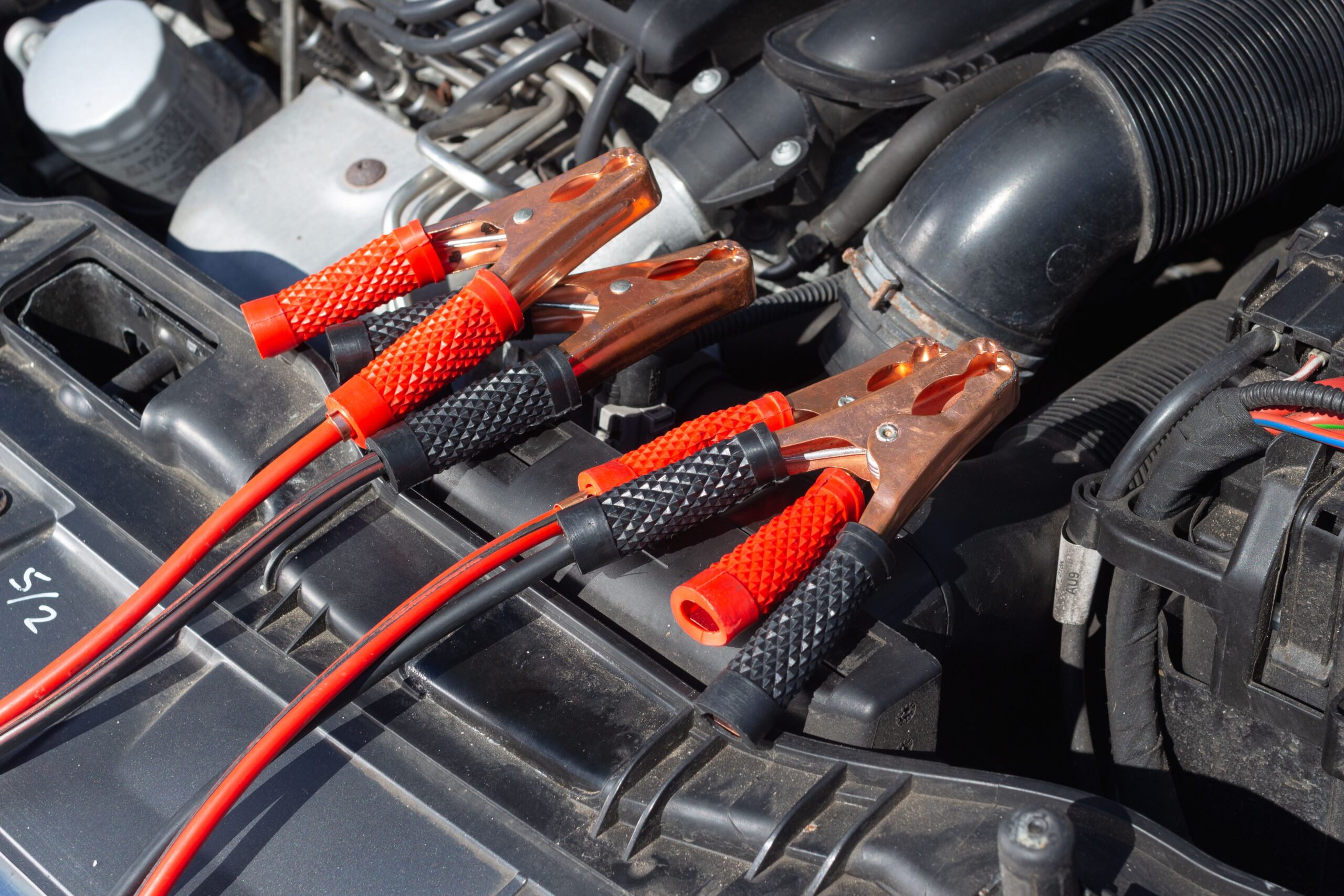 Close-up of jumper cable clamps connected to a car battery in an engine bay