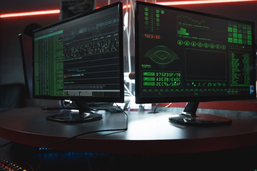 Dark room with dual monitors showing code, representing firewall exploitation campaigns in 2026